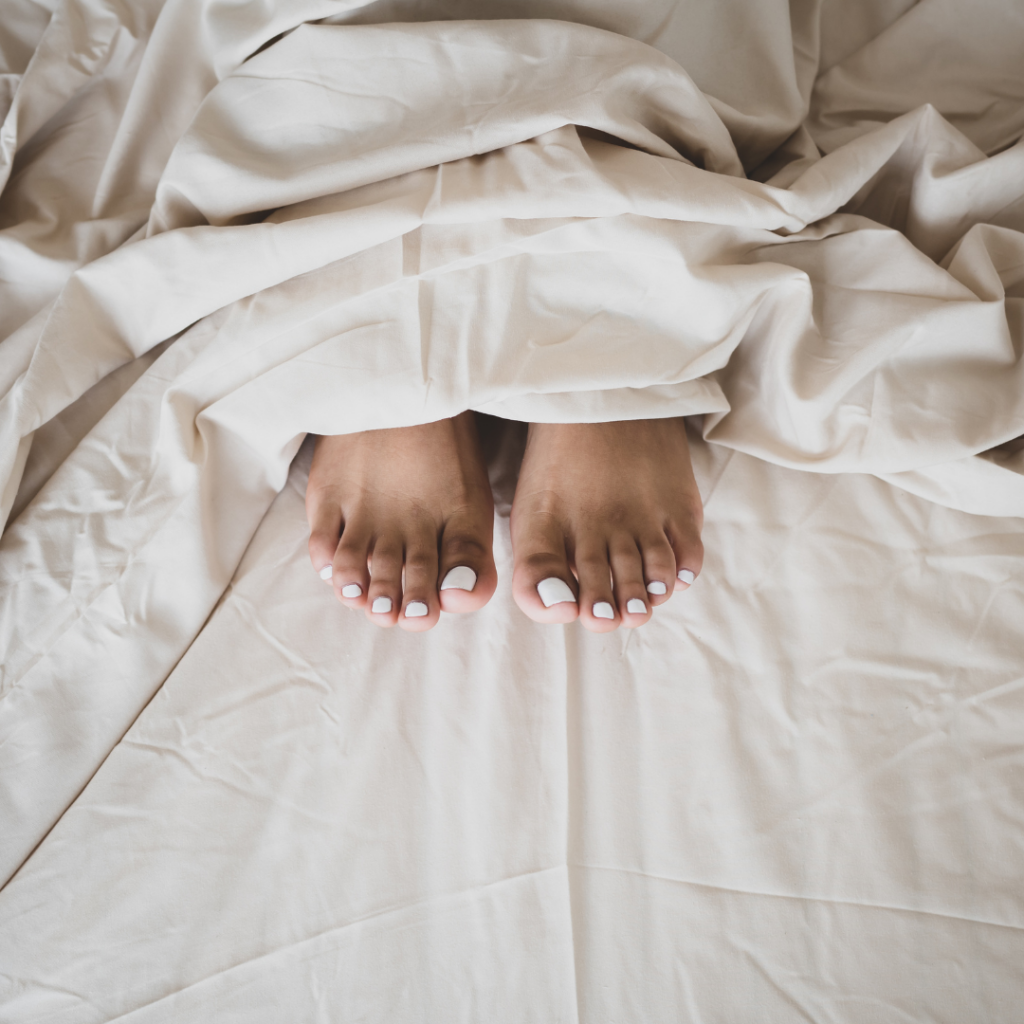 Gepflegte Füße mit weiß lackierten Zehennägeln nach einer Pedicure – entspannt im Bett präsentiert.